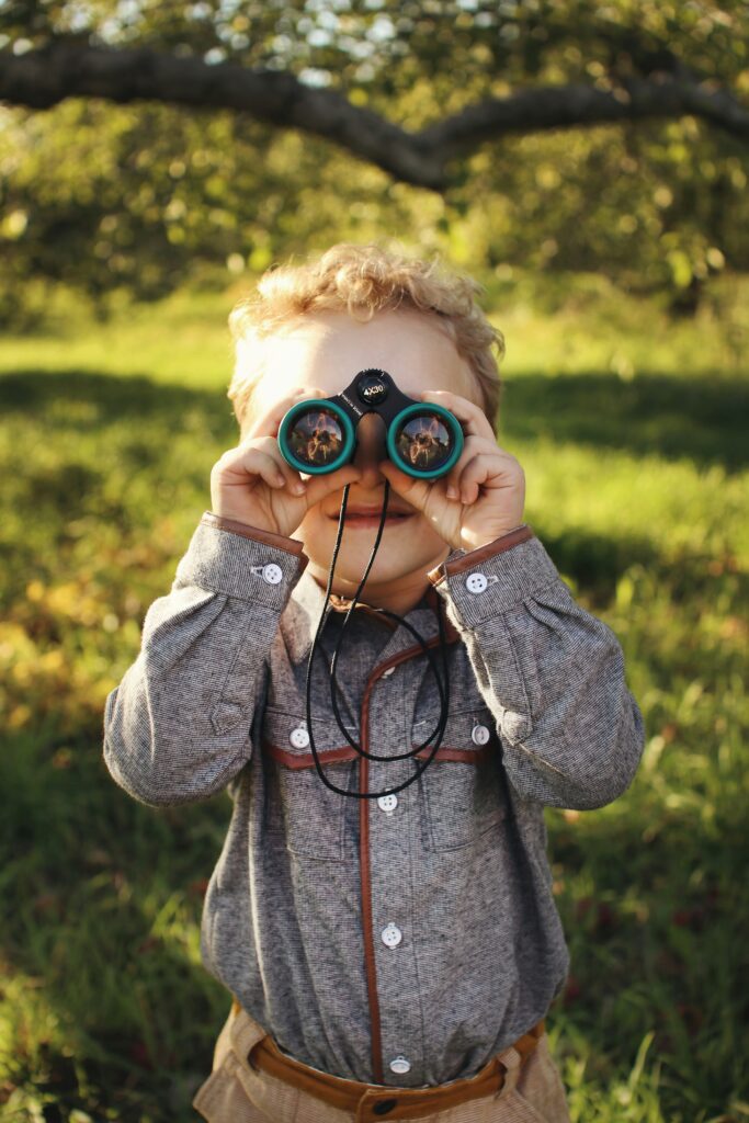A young boy peering through binoculars, smiling.